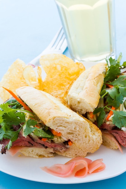 Sanduíche gourmet banh-mi com batatas fritas ao lado.