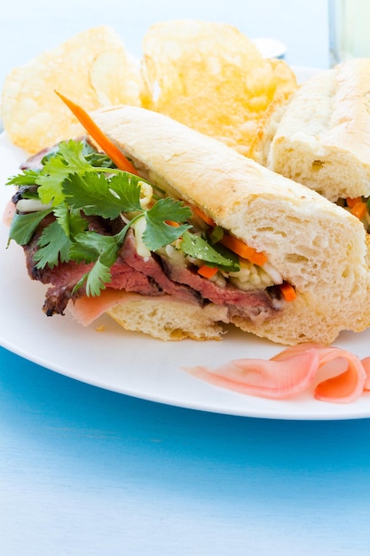 Sanduíche gourmet banh-mi com batatas fritas ao lado.