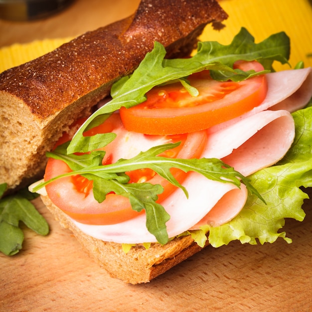 Sanduíche integral com presunto, tomate, latface e rúcula com copo de suco de laranja. Café da manhã