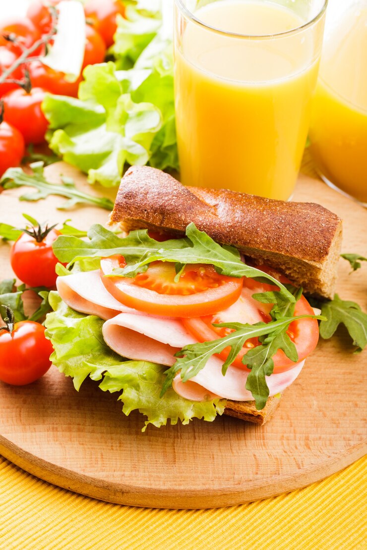 Foto sanduíche integral com presunto, tomate, latface e rúcula com um copo de suco de laranja no tabuleiro