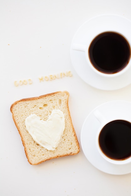 Sanduíche no café da manhã em forma de coração com sinal de bom dia de queijo e duas xícaras de café