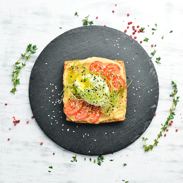 Sanduíche Pedaço fresco de ciabatta com tomates homus e ovo Café da manhã em uma placa de pedra preta