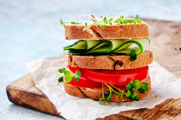 Sanduíche saudável caseiro com pão integral, pepino, tomate e micro ervas salada de agrião na placa de madeira.