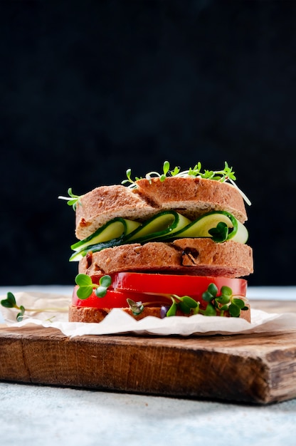 Sanduíche saudável caseiro com pão integral, pepino, tomate e micro ervas salada de agrião na placa de madeira.
