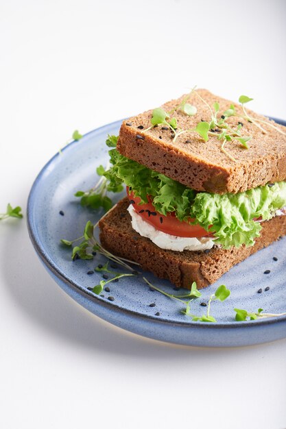 Sanduíche saudável com pão sem glúten, tomate, alface e microgreens germinados, polvilhados com sementes de gergelim servidas em prato