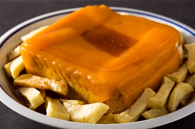 Sanduíche típico de francesinha portuguesa com batatas fritas no preto