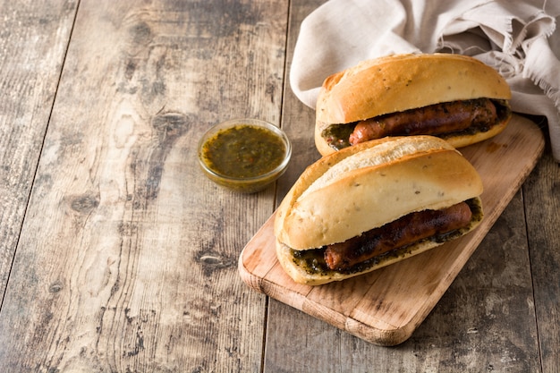 Sanduíche tradicional de Choripan Argentina com molho de chouriço e chimichurri na mesa de madeira