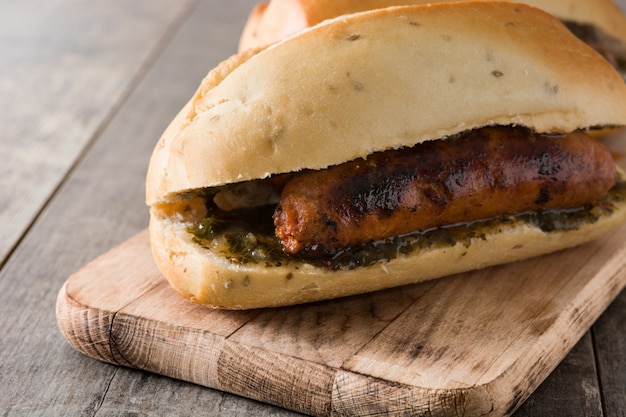 Sanduíche tradicional de Choripan Argentina com molho de chouriço e chimichurri na mesa de madeira