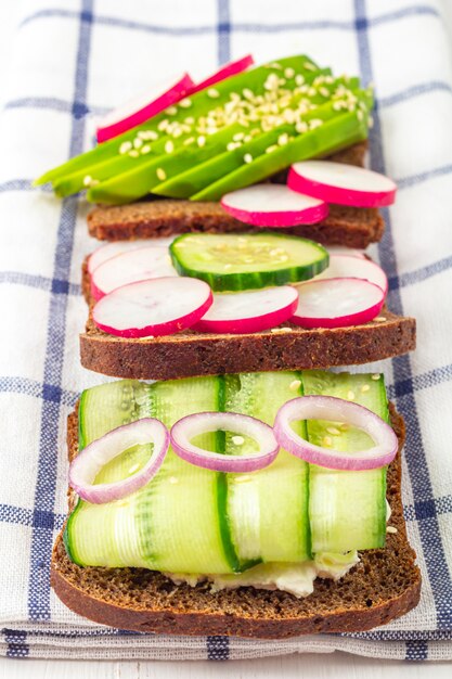 Sanduíche vegetariano de superalimento aberto com diferentes coberturas: abacate, pepino, rabanete em tecido. Alimentação saudável. Alimentos orgânicos e vegetarianos.