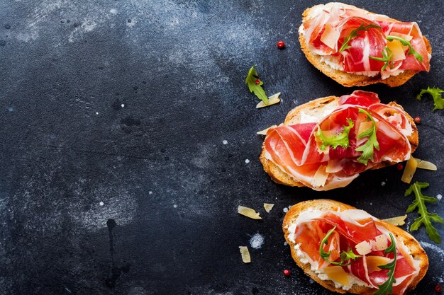 Sanduíches abertos com jamon, rúcula e queijo duro em uma superfície escura e velha de concreto