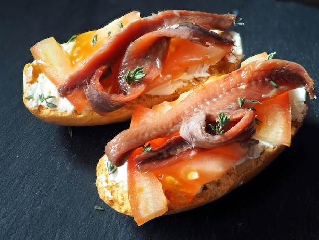 Sanduíches caseiros com fatias de tomate com queijo creme e anchovas em uma mesa de madeira preta Closeup