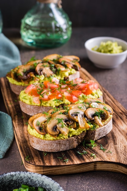 Sanduíches com abacate frito champignons tomates e ervas no pão de centeio em uma visão vertical de placa