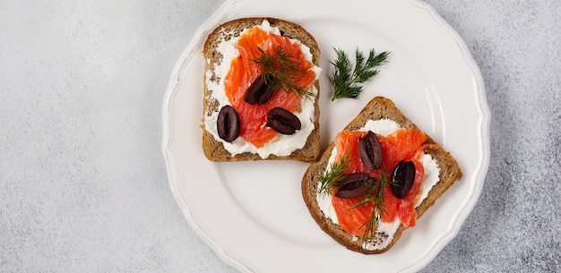 Sanduíches com azeitonas de salmão rosa fumadas, kalamata, microgreens e cream cheese na placa de cerâmica cinza e fundo de concreto na moda. brinde tradicional escandinavo. vista do topo.