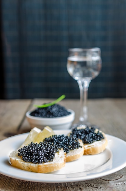 Foto sanduíches com caviar preto e copo de vodka