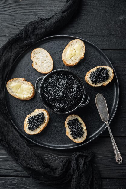 Sanduíches com caviar preto, no fundo preto da mesa de madeira, vista superior plana lay