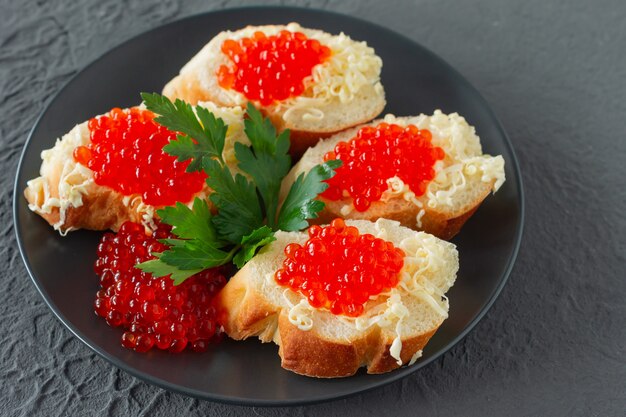 Sanduíches com caviar vermelho, limão e salsa na placa preta sobre fundo de concreto. frutos do mar.