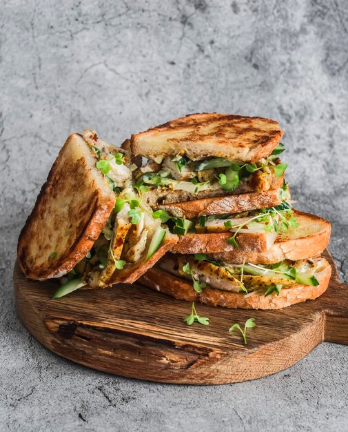 Sanduíches com microgreens de pepino de frango frito açafrão e molho de maionese de mostarda caseiro em uma tábua de madeira em um fundo cinza