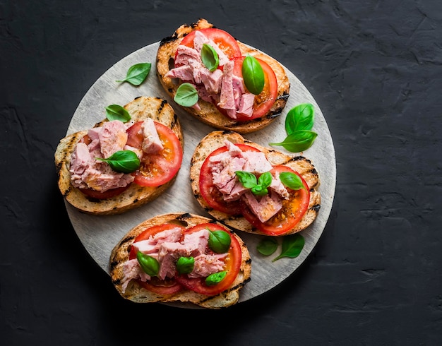 Sanduíches com tomate manjericão e atum na tábua de madeira em fundo escuro