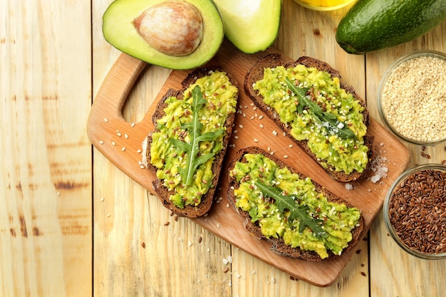 Sanduíches de abacate e rúcula e outros ingredientes em uma mesa de madeira natural. Sanduíche com purê de abacate. vista de cima