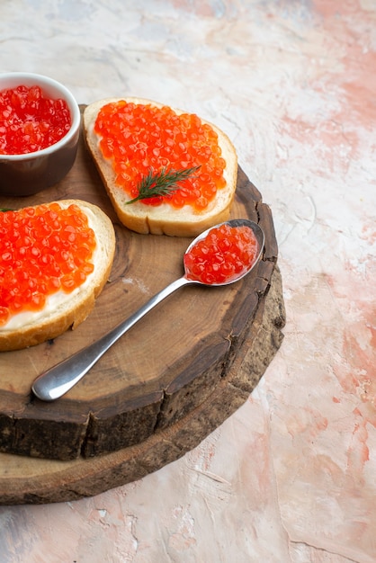 sanduíches de caviar de vista frontal com talheres na superfície da luz da placa de corte