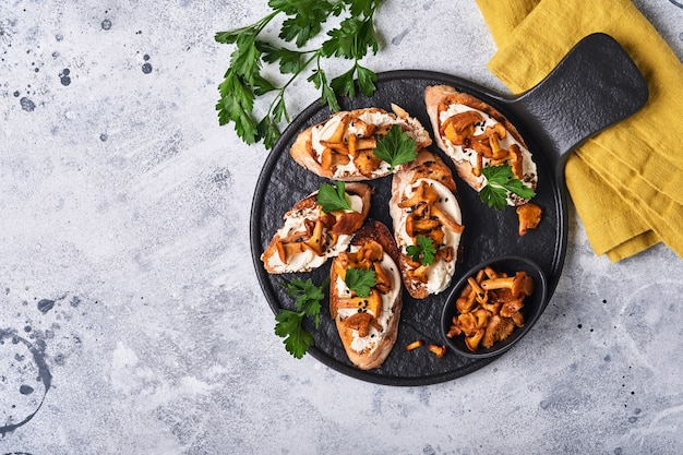 Sanduíches de chanterelle com queijo. Sanduíche aberto com queijo cremoso, temperos e pimenta e salsa fresca em um velho fundo de madeira. Brincar. Vista do topo.