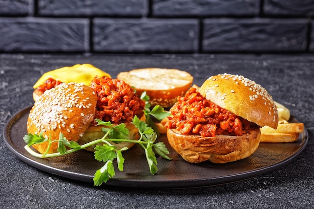 Sanduíches de churrasco Sloppy Joe com batatas fritas em uma placa preta com uma parede de tijolos ao fundo, close-up, cozinha americana