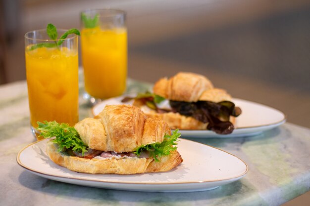 Sanduíches de croissant cozido fresco com presunto e alface ao lado de limonada de frutas na mesa de mármore