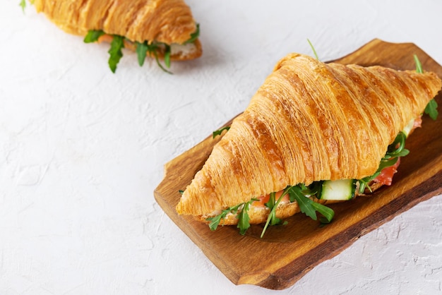 Sanduíches de croissants crocantes com pepino de queijo creme de peixe salmão e rúcula em uma placa de madeira