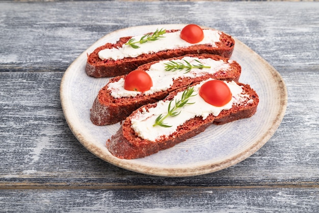 Sanduíches de pão de beterraba vermelha com cream cheese e tomate em madeira cinza