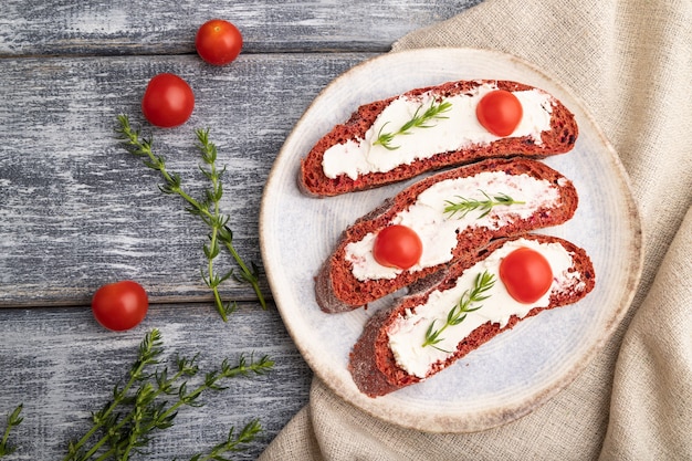 Sanduíches de pão de beterraba vermelha com cream cheese e tomate em madeira cinza