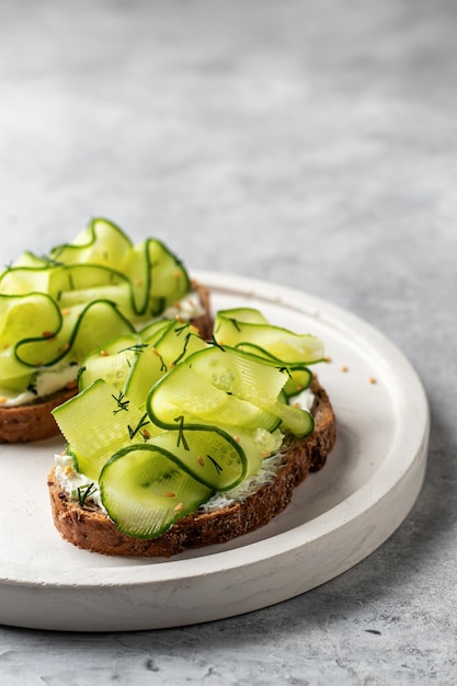 Sanduíches de pepino com queijo macio fecham para um delicioso café da manhã vegetariano saudável em fundo cinza com espaço de texto