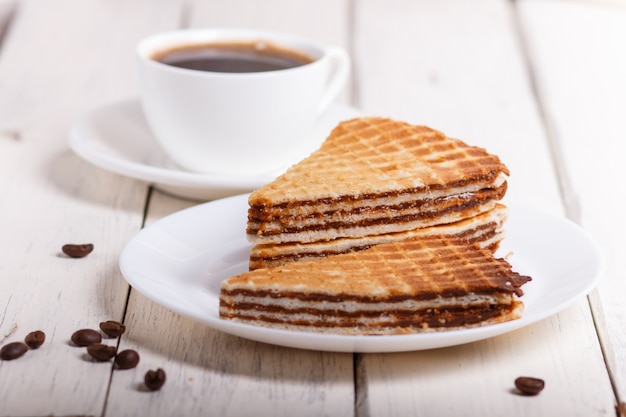 Sanduíches do waffle com leite condensado fervido na placa na tabela de madeira branca com xícara de café.