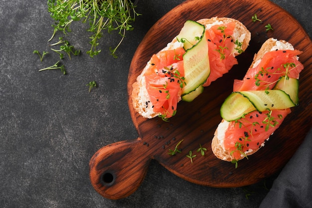 Sanduíches torrada de salmão com cream cheese pepino gergelim preto e microgreens em fundo preto frutos do mar comida saudável fotografia em low key vista superior