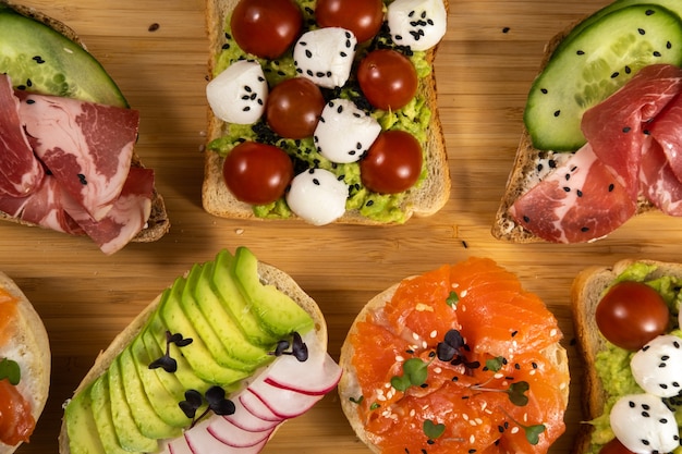 Sanduíches variados com peixes, queijos, carnes e vegetais espalhados pelo tabuleiro