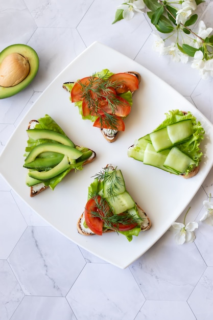 Sanduíches vegetarianos com abacate, tomate e pepino em um fundo claro