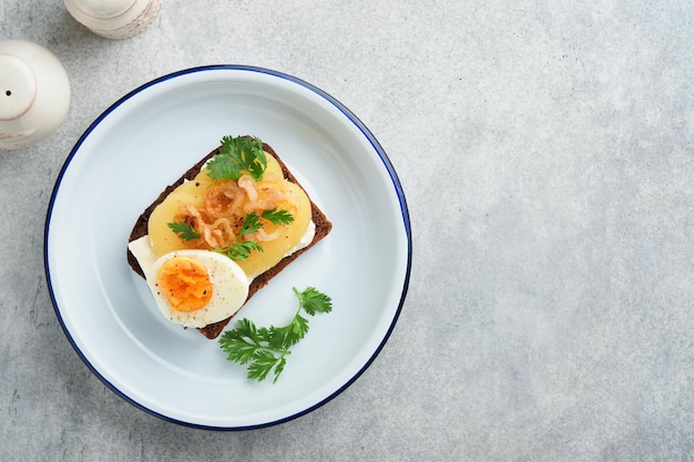 Sándwich abierto o smorrebrod con pan de centeno, huevos de arenque, cebollas caramelizadas, perejil y requesón sobre fondos de mesa rústica de madera antigua Comida tradicional danesa o escandinava