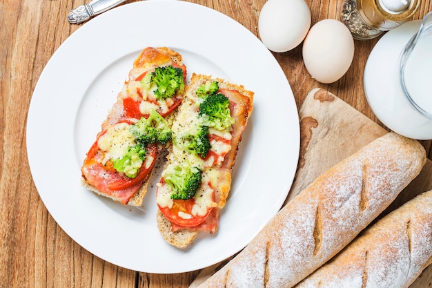 Sándwich abierto con prosciutto, mozzarella y tomates en la mesa de la cocina, enfoque superficial