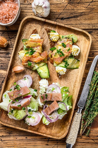 Sándwich abierto con salmón y arenque, queso crema y ensalada sobre una tabla para cortar