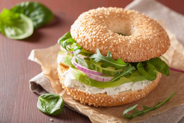 Sandwich de aguacate en bagel con rúcula de pepino y cebolla con queso crema