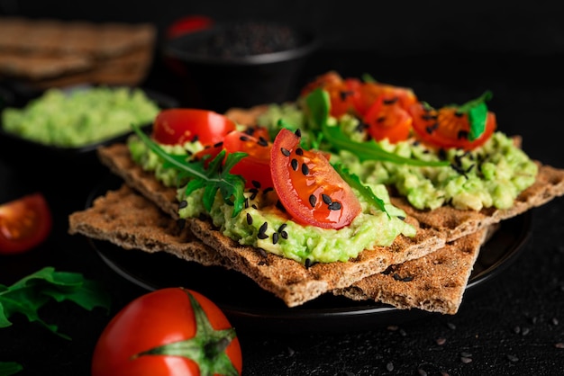 Sándwich de aguacate con crema de aguacate y pan crujiente de centeno para la merienda. Fibra, fitness y alimentos dietéticos. Pan de centeno con guacamole, rúcula y tomates cherry sobre fondo oscuro. foto de alta calidad