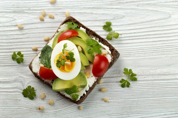 Sandwich con aguacate, huevo, tomate, queso, perejil, hojas de ensalada.