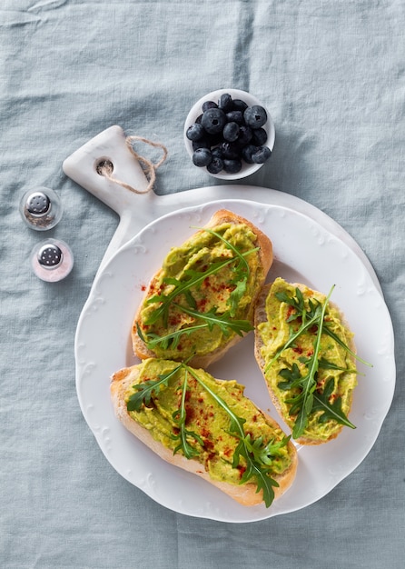 Sandwich de aguacate y rúcula con pimentón sobre la mesa. Desayuno o merienda saludable en un plato sobre un mantel de lino azul