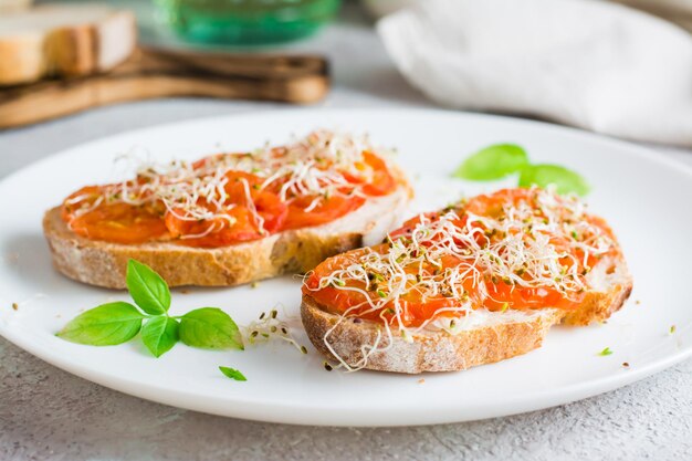 Sándwich apetitoso con tomates secos y brotes de trébol y alfalfa en un plato sobre la mesa Dieta alimentos orgánicos Primer plano