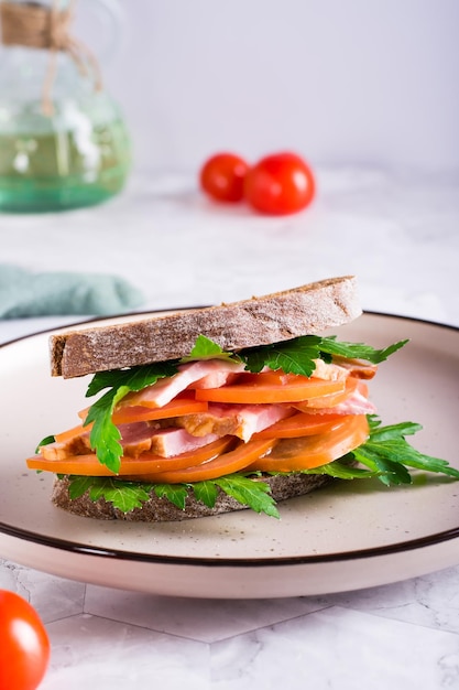 Sandwich aus Roggen-Ciabatta-Schinkentomaten und Petersilie auf einem Teller auf dem Tisch Vertikale Ansicht