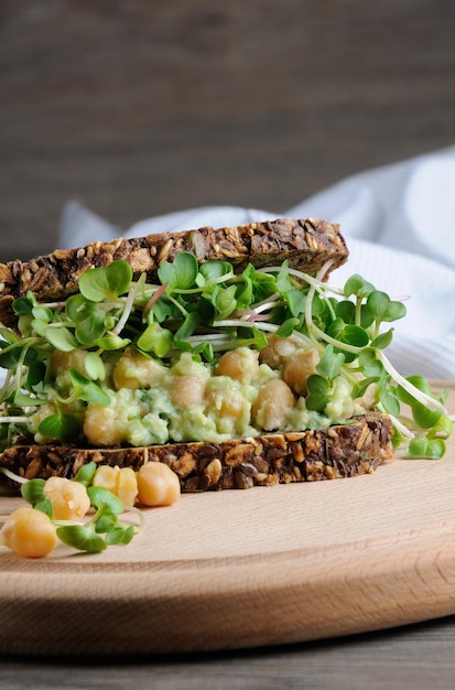 Sandwich aus Roggenbrot mit Müsli mit zerstoßenen Avocado-Kichererbsen und Rettichsprossen