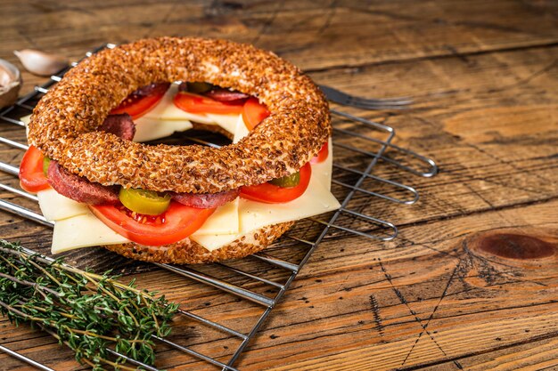 Sándwich de bagel con lechuga, tomate, queso amarillo y salchichas. Fondo de madera. Vista superior. Copie el espacio.