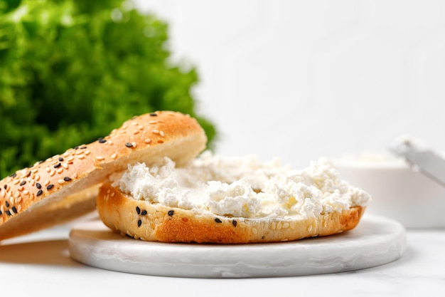 Sándwich de bagel con queso crema sobre tablero de mármol y fondo blanco