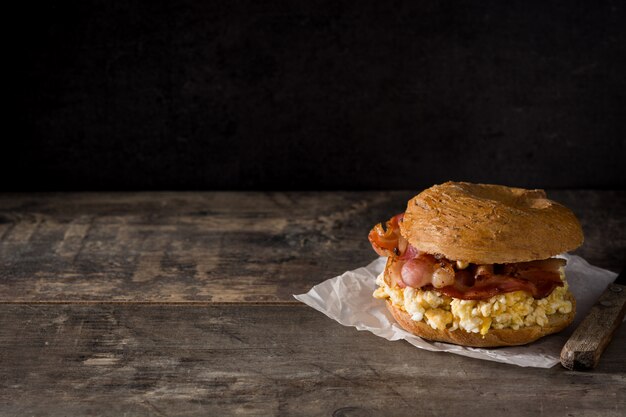 Sándwich de bagel con tocino, huevo y queso en el espacio de copia de mesa de madera