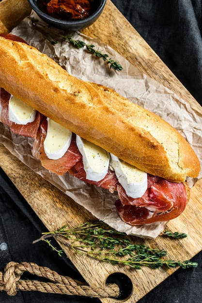 Sándwich de baguette con jamón serrano, paleta ibérica, queso Camembert en la tabla de cortar.