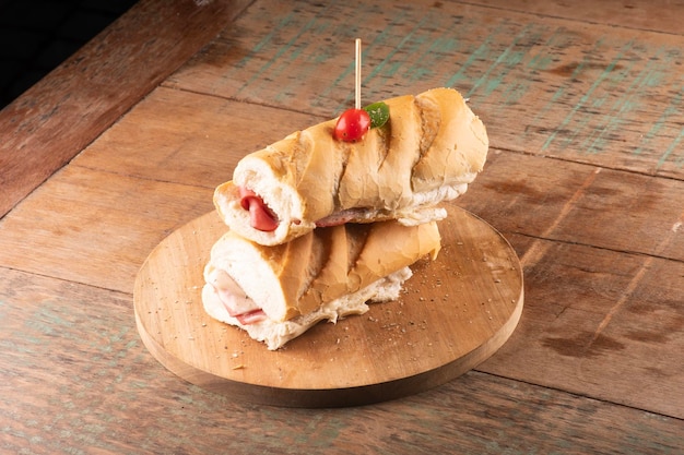 Sándwich de baguette con mortadela y queso mozzarella y tomates cherry sobre una mesa de madera de fondo borroso a cielo abierto